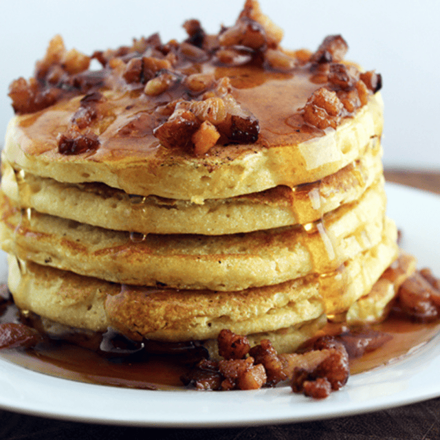 stack of pancakes with bacon bits and syrup on top