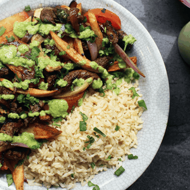 beef, onions, tomato, French fries, rice, green sauce on a plate
