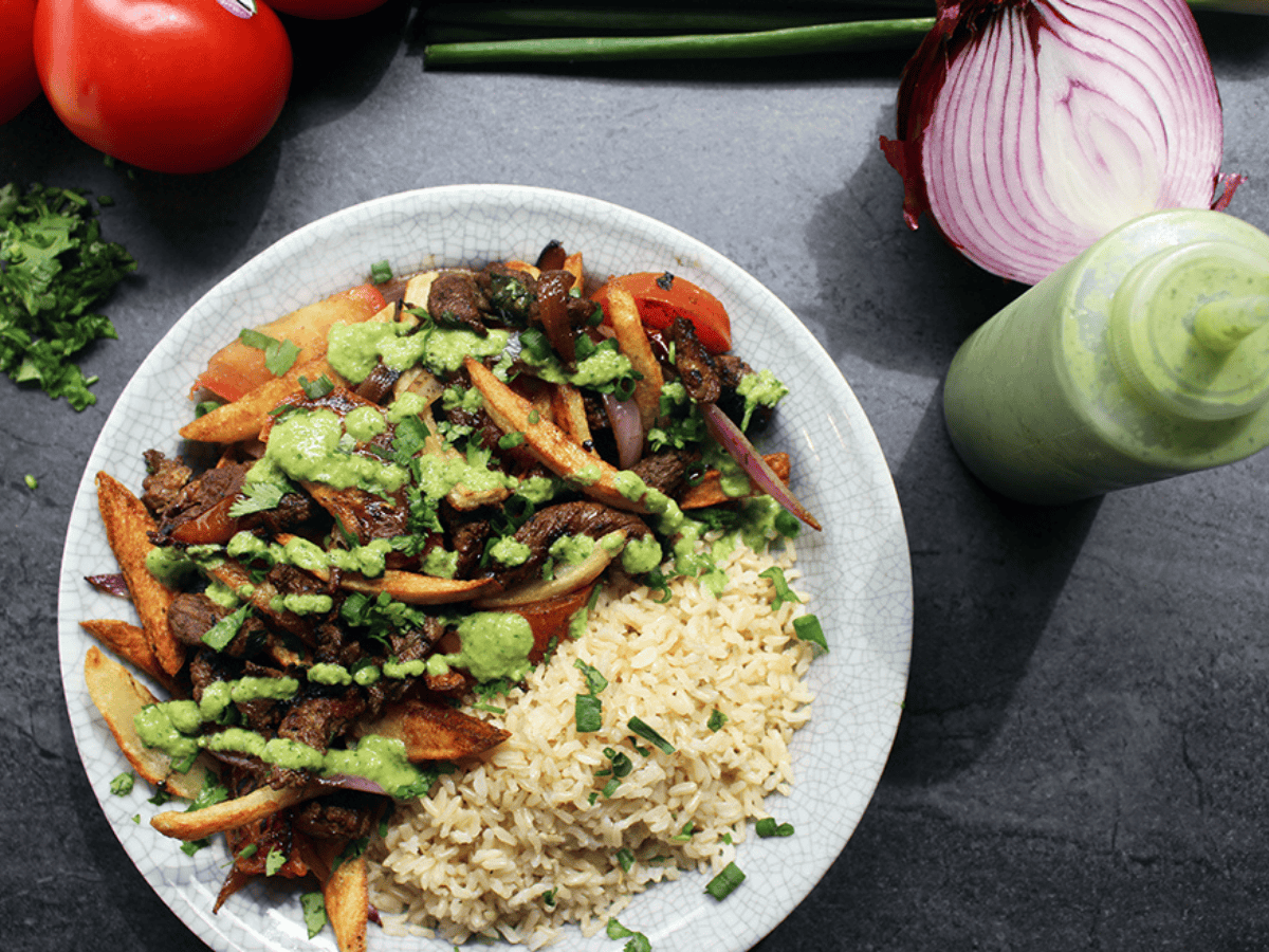 beef, onions, tomato, French fries, rice, green sauce on a plate