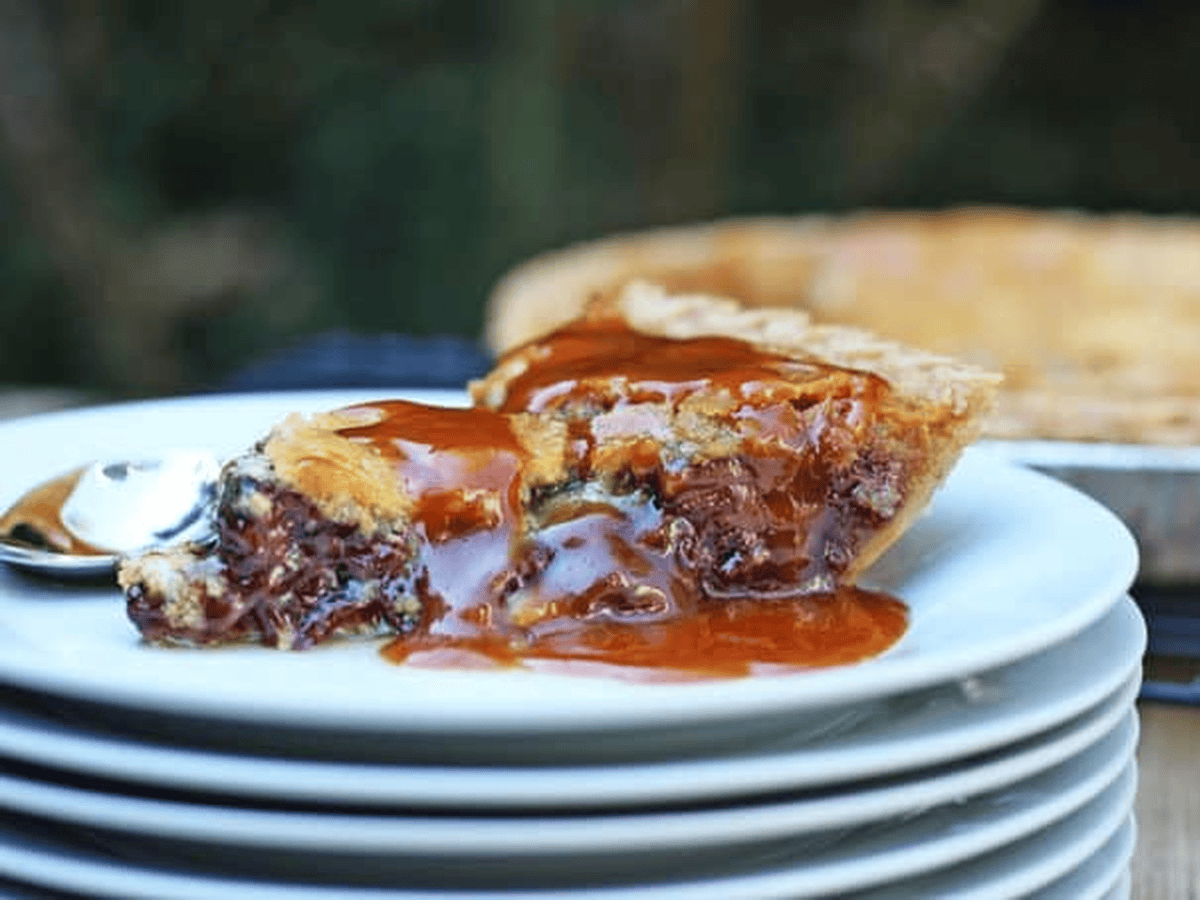 Slice of pie with chocolate chip and caramel on stack of plates