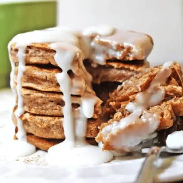 stack of pancakes with icing on a white plate with a fork