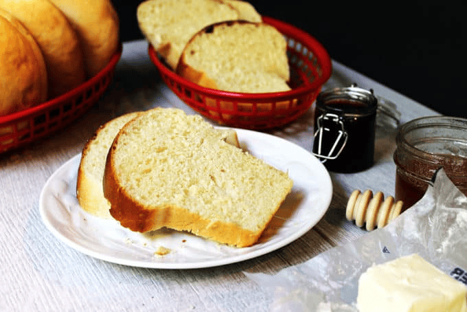 Bread on a plate and in baskets with jelly, butter, and honey on the side