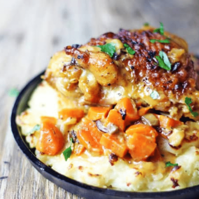 Carrots and chicken thighs on top of mashed potatoes