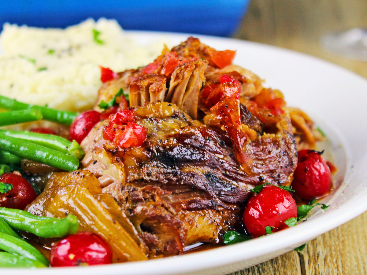 cooked pork on a white plate with cherries and green beans