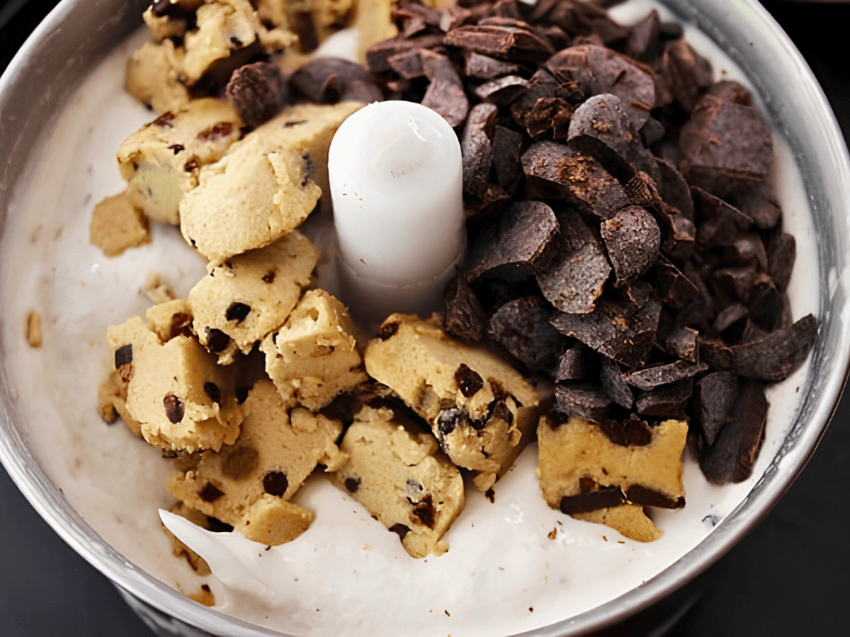 pieces of unbaked dough and cocoa on top of bed of ice cream inside ice cream maker