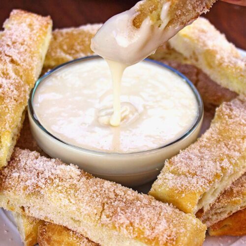 Dominos Cinnastix with Dipping Sauce finished bread sticks on plate surrounding bowl of icing.