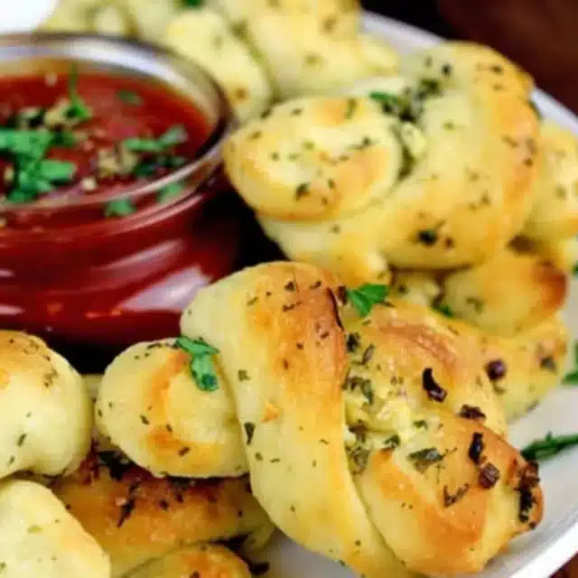 Twisted bread with garlic and herb garnish, served with red dipping sauce