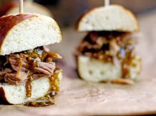 Tender Pulled Pork covered in a homemade raspberry honey mustard sauce with whole mustard seeds served in a toasted pretzel roll. Perfect for your tailgate or gameday party.