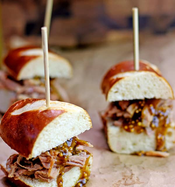 Tender Pulled Pork covered in a homemade raspberry honey mustard sauce with whole mustard seeds served in a toasted pretzel roll. Perfect for your tailgate or gameday party.