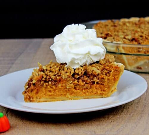 Slice of creamy pumpkin pie topped with streusel and cream.