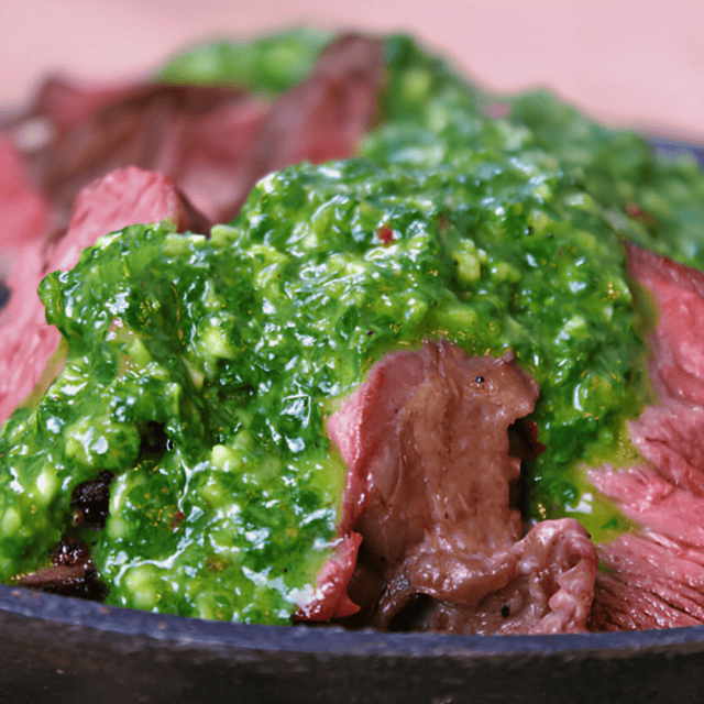 slices of meat on a plate with green sauce poured over