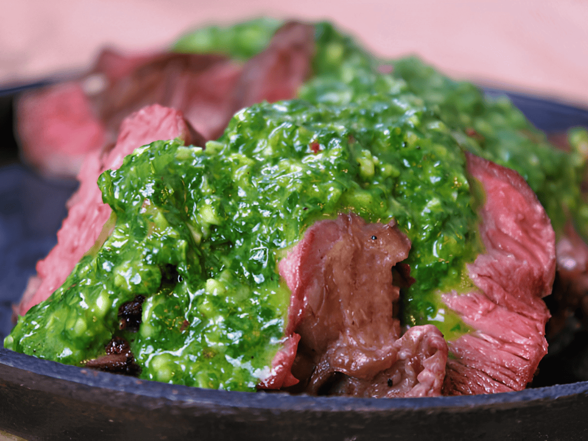 slices of meat on a plate with green sauce poured over