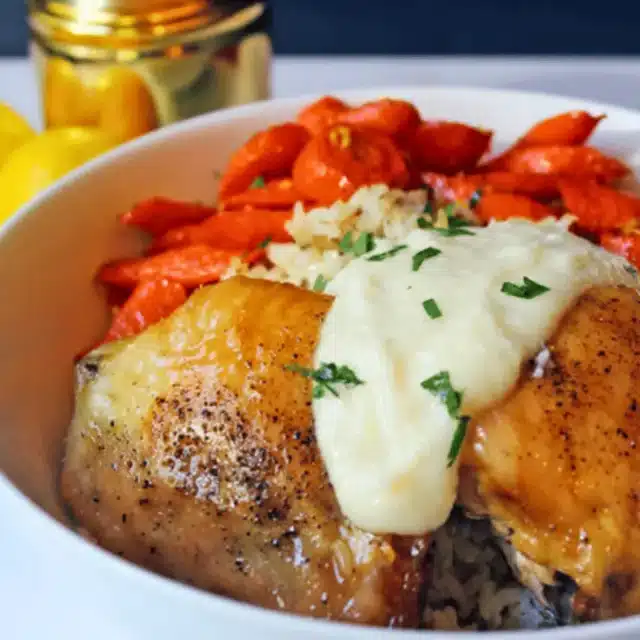 Bowl of cooked chicken thighs with veggies and garlic sauce