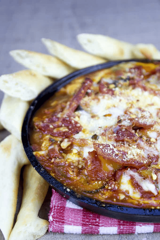 Pizza dip in a cast iron skillet with bread sticks on the side