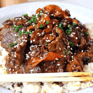 hot and tangy meat on top of a bed of rice with veggies on top