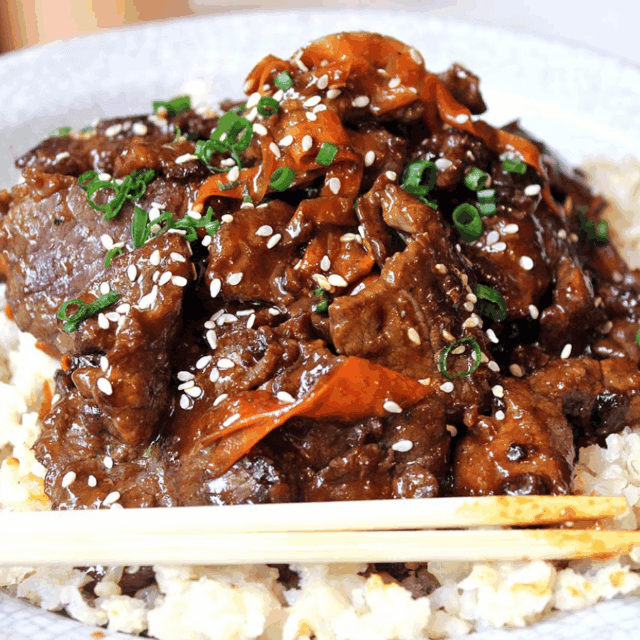 hot and tangy meat on top of a bed of rice with veggies on top