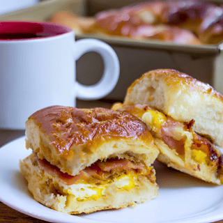 two small breakfast sandwiches on a white plate with a coffee mug on the table