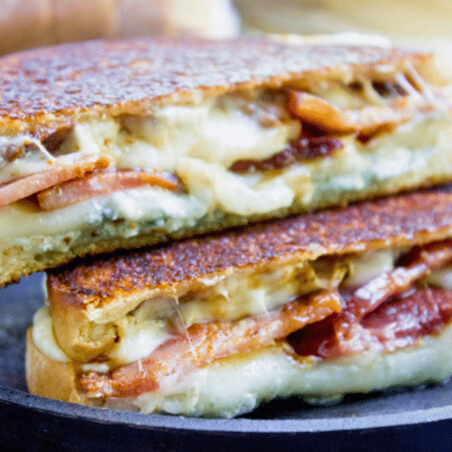 dairy, fruit, and pig meat heated inbetween bread cut in half on top of plate