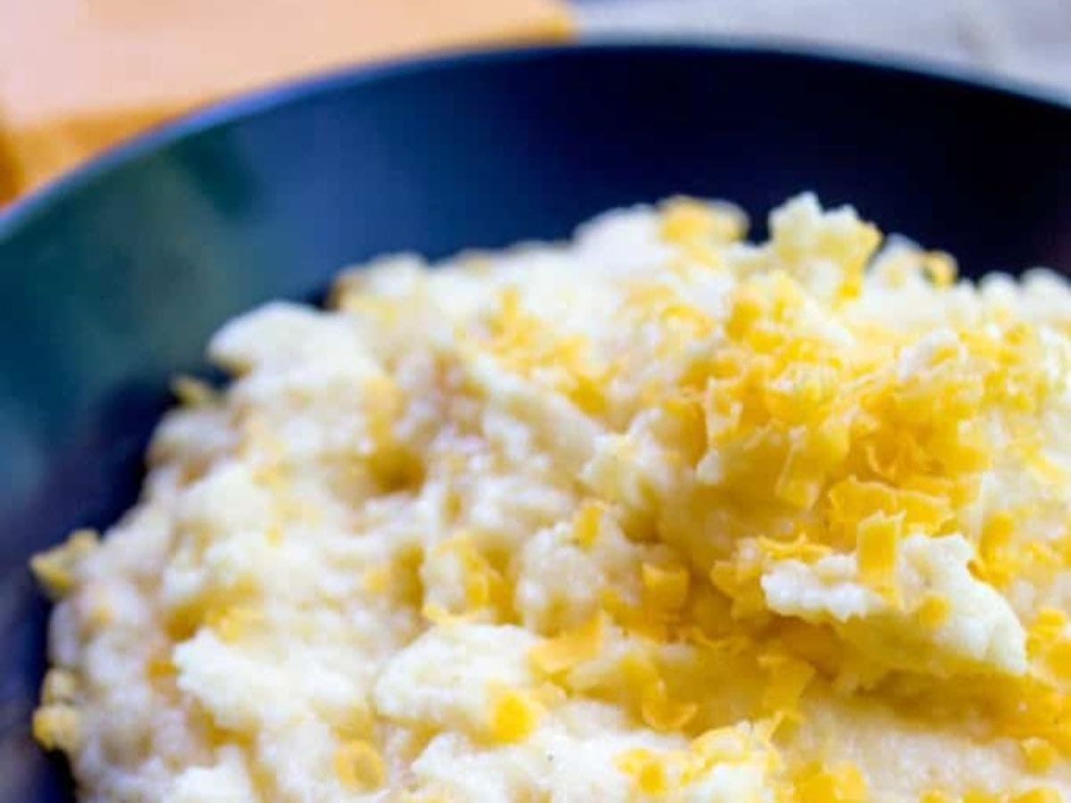 Oven Baked Creamy Cheese Polenta made with just four ingredients and none of the danger associated with boiling, bubbling hot polenta on the stove you have to keep stirring! Polenta in a blue bowl, ready to serve.