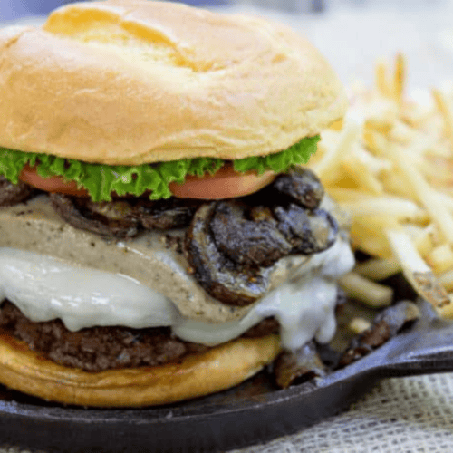 Burger with truffle mousse and mushrooms on metal skillet with fries in the backround