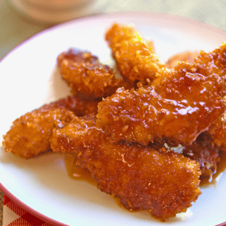 crispy sticky chicken strips on a white plate