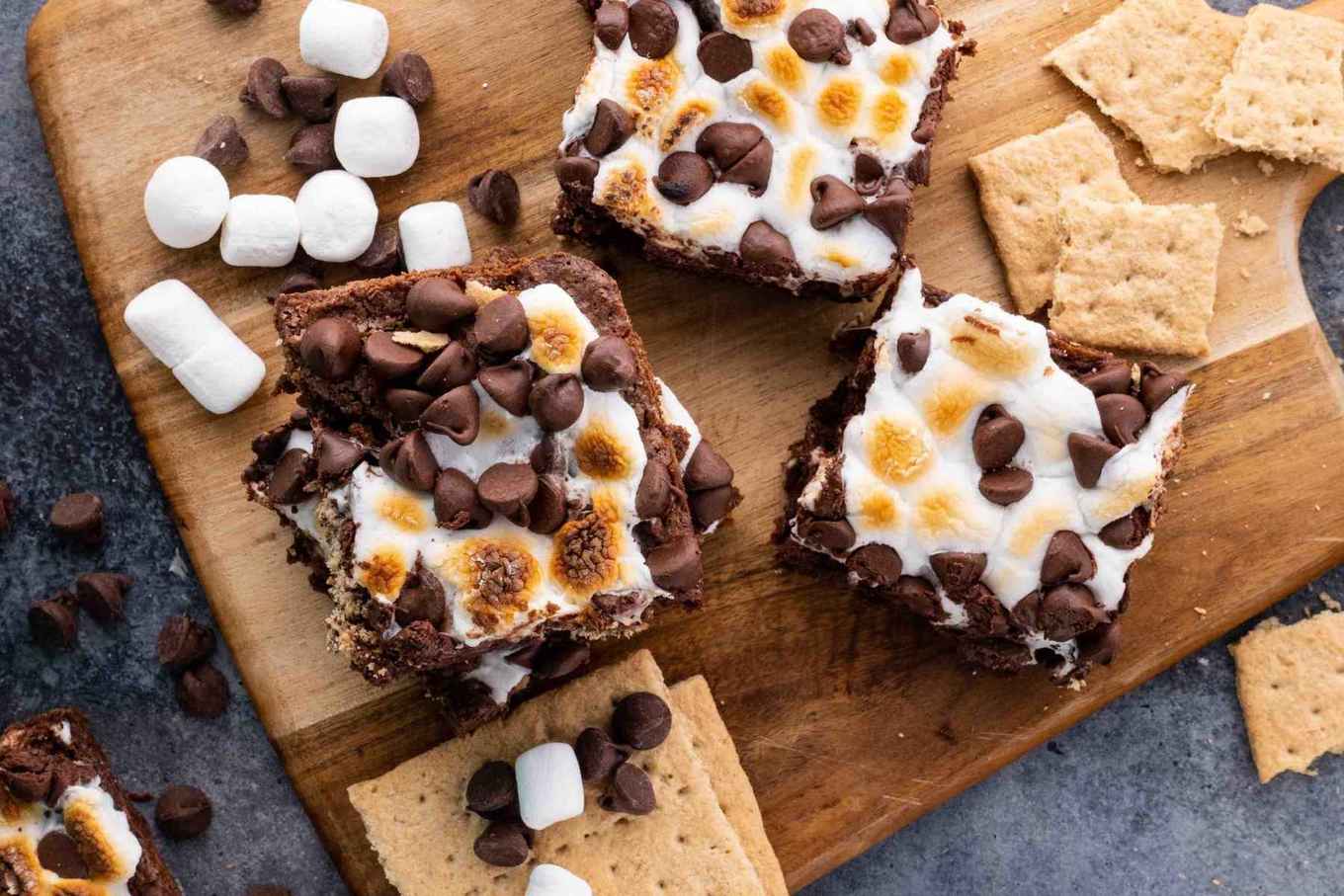 S'mores Brownies stacked on cutting board with graham crackers and marshmallows