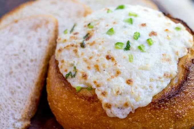 artichoke dip with cream cheese bubbling out of baked bread bowl