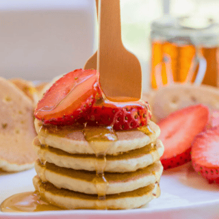 small circle hotcakes stacked on one another with strawberries and syrup drizzled on top