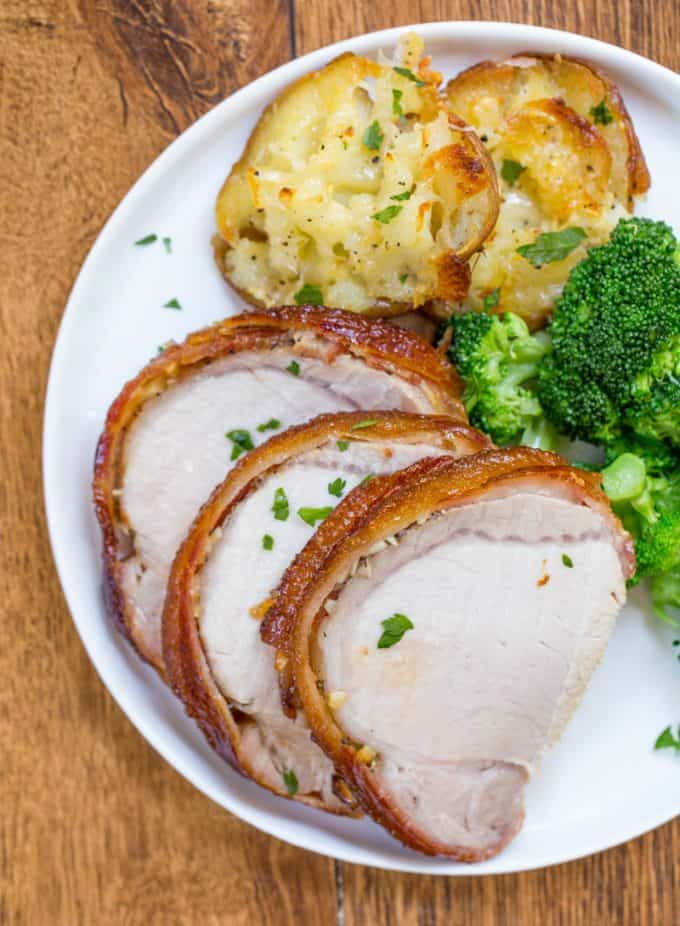 Slow Cooker Pork Loin wrapped in bacon on serving dish with vegetable sides