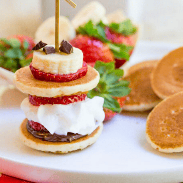 Bites stacked with strawberries and whipped cream with small pancakes