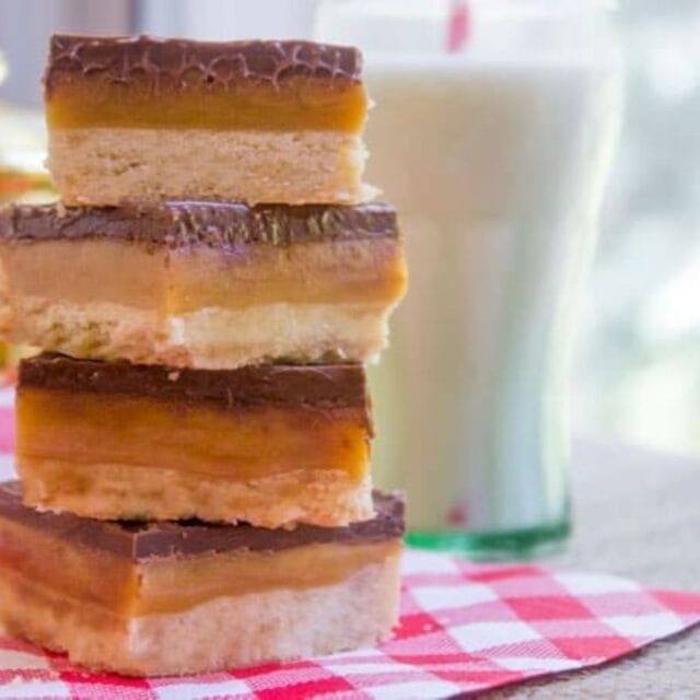 A stack of bars and a glass of milk on a red and white checkered cloth.