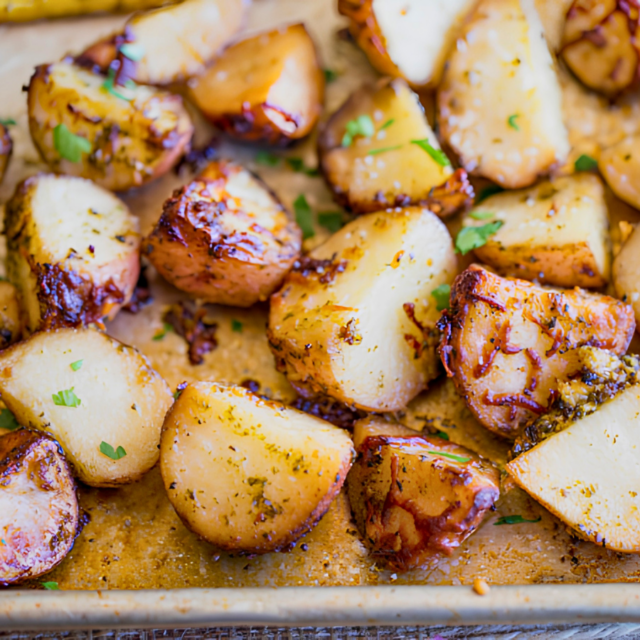 side view of cut up potatoes covered in cheese and greens on baking sheet