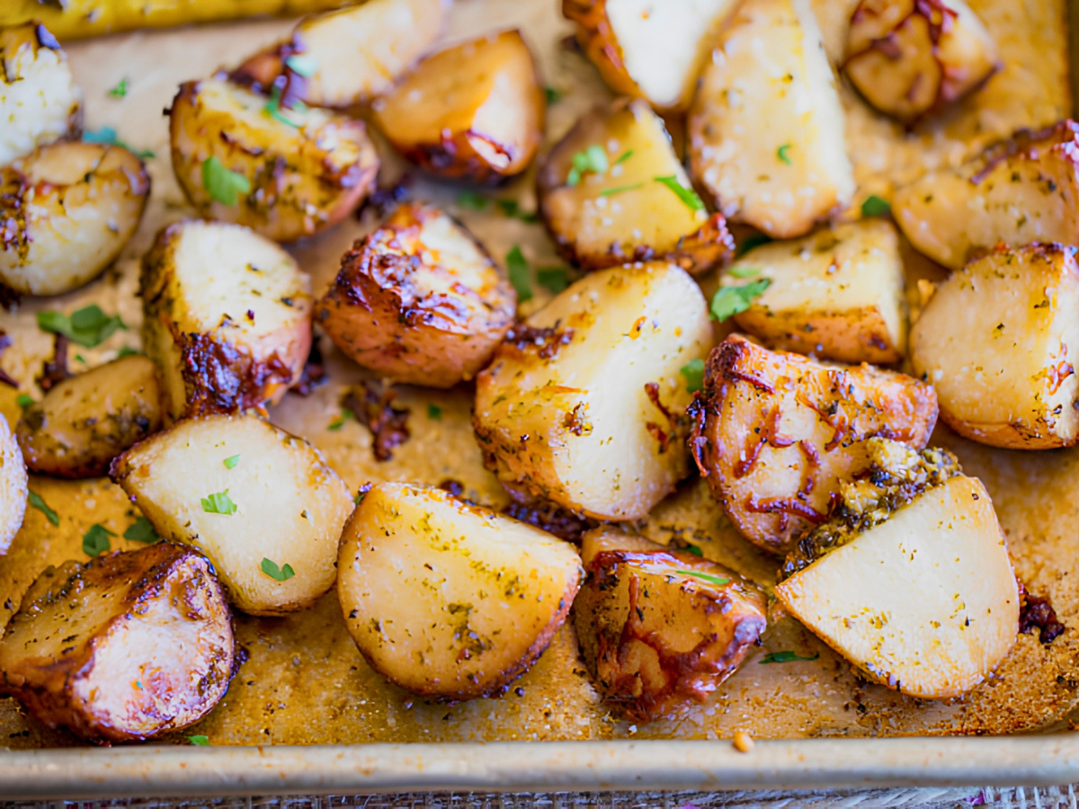 side view of cut up potatoes covered in cheese and greens on baking sheet