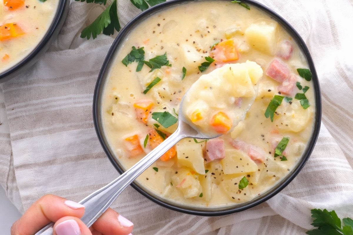 Slow Cooker Ham and Potato Soup in bowl with parsley garnish and spoon bite