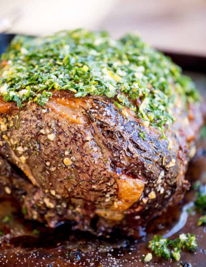 Perfect Garlic Prime Rib made with a garlic, thyme and rosemary crust is gorgeously browned on the outside and a perfect medium on the inside. Topped off with a gremolata it is the perfect show-stopping holiday/event meal! unsliced Prime Rib with herb topping