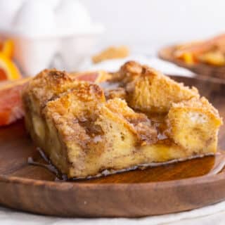 Side view of baked French Toast on wood plate with orange slice