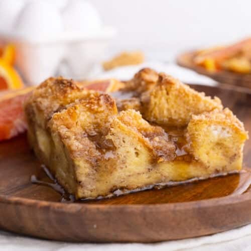 Side view of baked French Toast on wood plate with orange slice