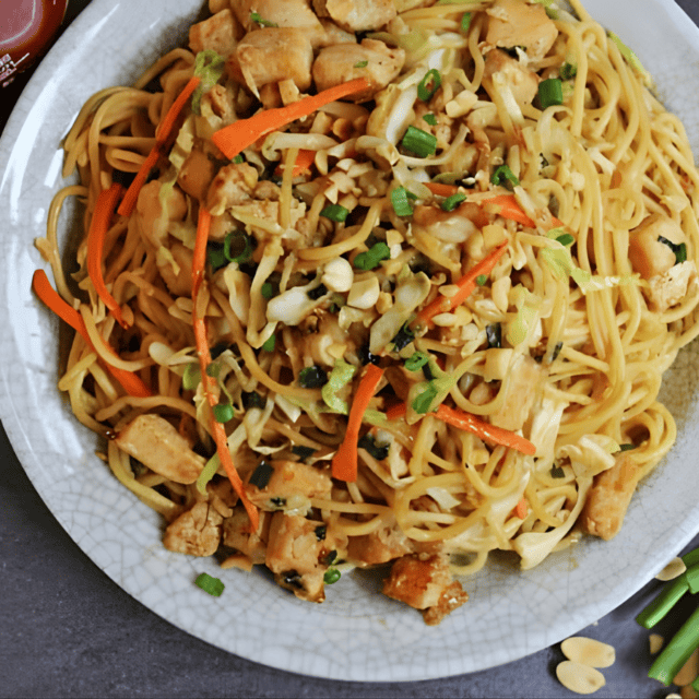 aerial view of cooked poultry, tofu, and veggies with noodles on a plate with green garnish