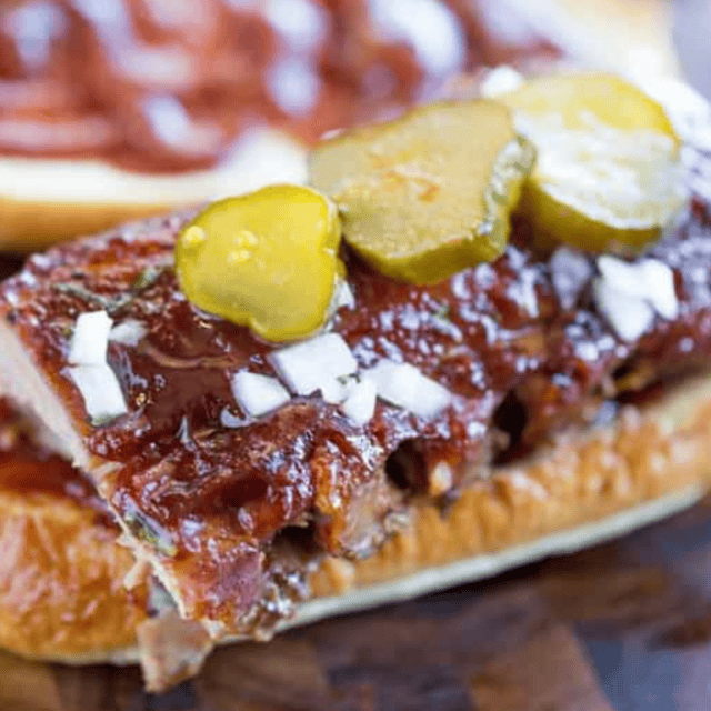 Sandwich with rib meat on a table topped with pickles and white onion