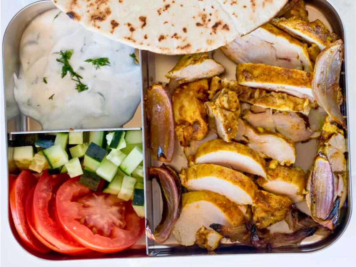 Bento box with chicken, vegetables, sauce, and pita
