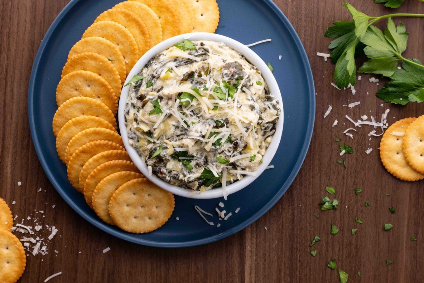 Slow Cooker Spinach Artichoke Dip in bowl on serving plate with crackers