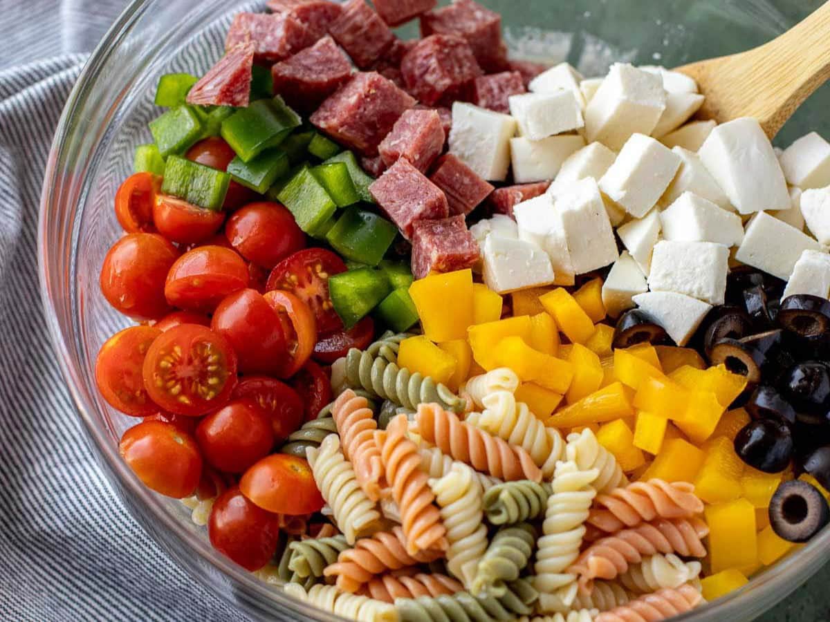 Veggies, pasta, cheese, and salami unmixed in bowl.