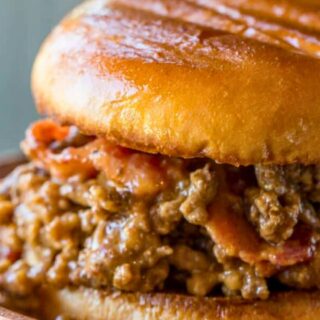 Close up of beef and bacon sandwich on a wooden plate