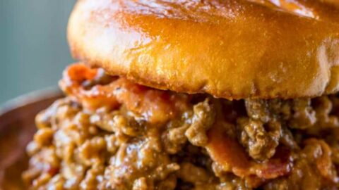Close up of beef and bacon sandwich on a wooden plate