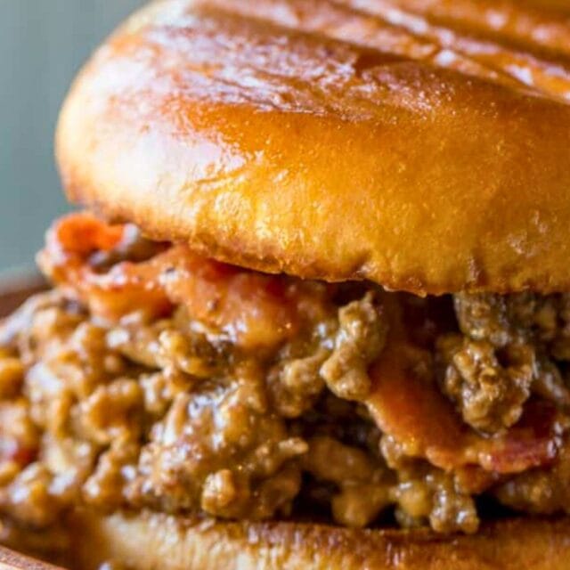 Close up of beef and bacon sandwich on a wooden plate