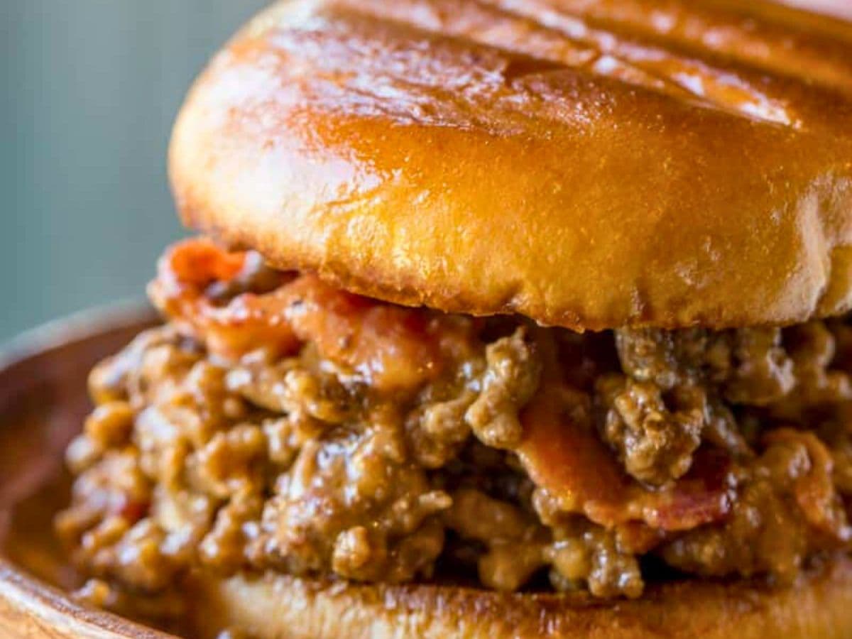 Close up of beef and bacon sandwich on a wooden plate