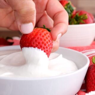 Homemade Cool Whip in bowl with strawberry dipping
