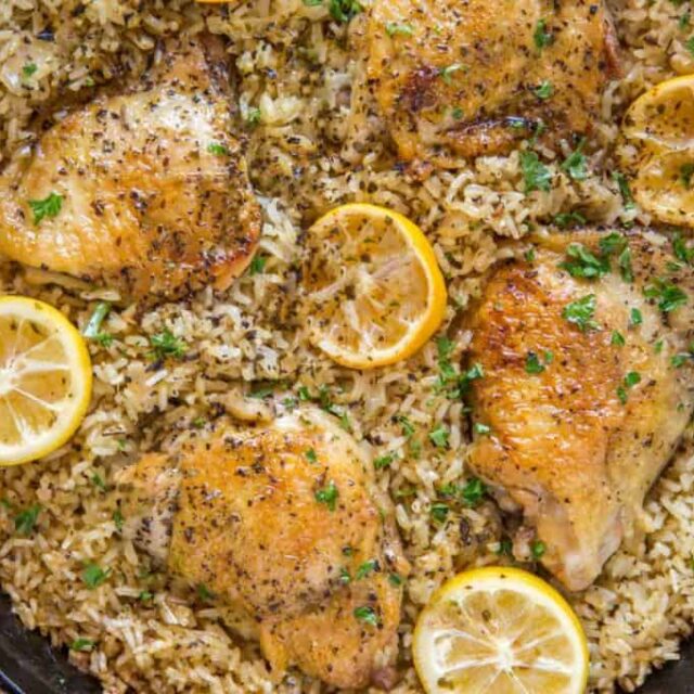 cast iron skillet with chicken, rice, and lemon halves