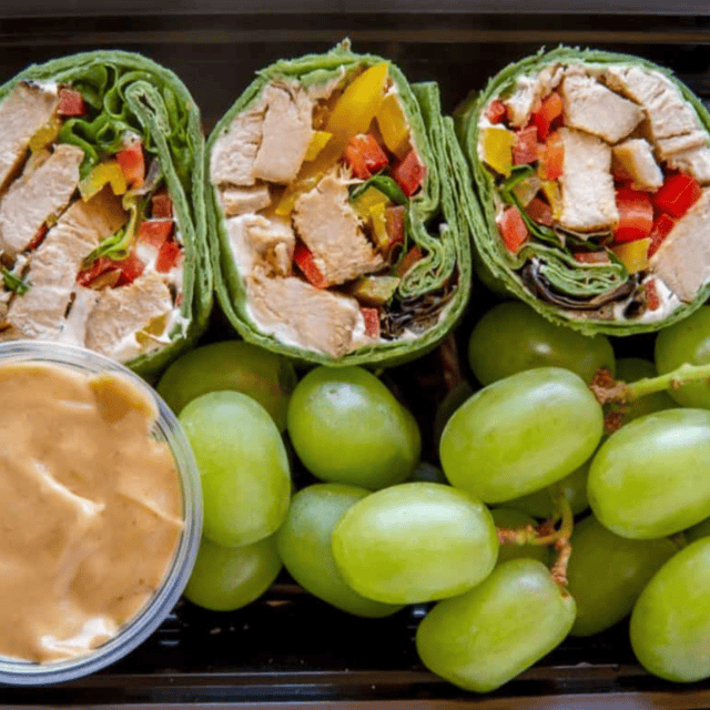 Wraps in a meal prep container with dipping sauce and grapes