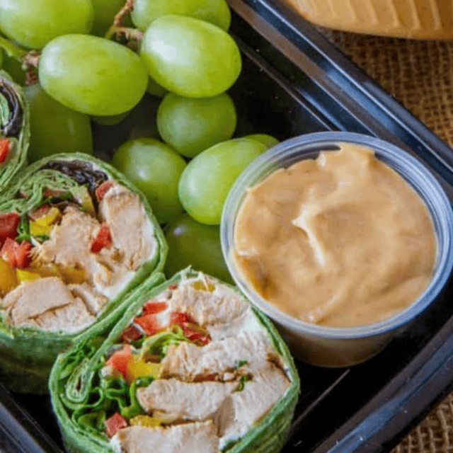 Close up of chicken wrap, sauce, and grapes in a meal prep container